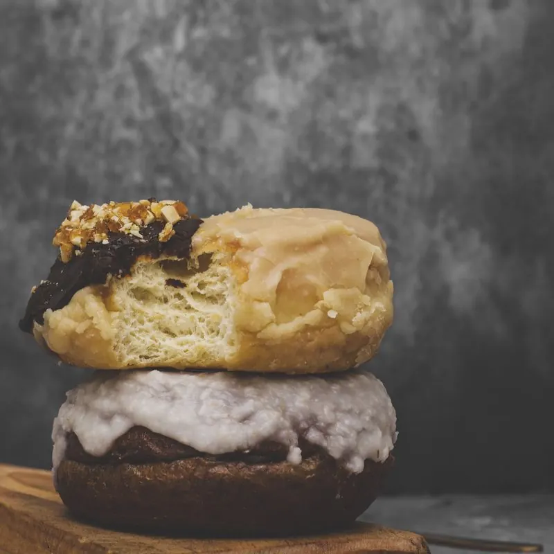 Dos donas apiladas sobre una tabla, la de arriba cortada: se ve la miga de la masa brioche